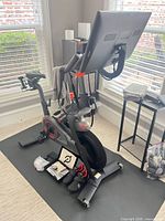 Full view of Peloton Bike+ on floor mat with accessories positioned at base