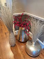 Three vases arranged together displaying differing shapes, finishes, and included florals