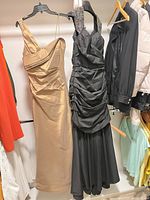 Full view of both dresses hanging: champagne-gold one-shoulder and black beaded halter
