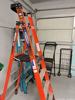 Red Werner Podium ladder, blue ladder, black step stool, folded wire cart