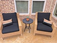 Two wicker chairs, cushions, pillows and side table arranged together
