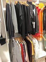 Full rail of assorted black, gingham, colour-block and orange garments on hangers