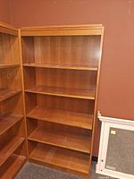 Front view of two similar oak veneer bookcases, showing the lot bookcase’s shelves and finish