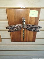 Front view of brass dragonfly door knocker on wood backing
