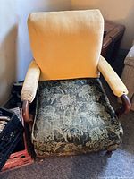 Front view of armchair showing yellow backrest, floral seat cushion, carved wood arms and legs