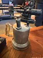 Side view antique metal blow torch showing wooden handle and fittings