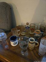 Mixed drinkware on table including plastic tumbler, ceramic and glass steins, printed glass