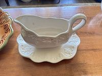 Side view of white embossed ceramic gravy boat on underplate