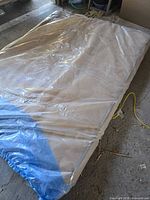 Full view of mattress in plastic wrap on garage floor