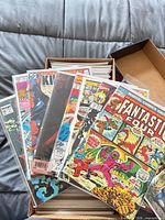 Open box containing stacks of bagged comic books; front issues Fantastic Four, X-Men, Amazing Spider-Man visible