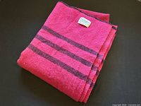 Folded magenta wool blanket showing triple dark stripes and edge finish