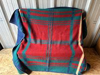 Front view of unfolded plaid fleece blanket showing red dominant side with green, navy and cream plaid pattern