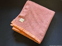 Folded rust orange wool blanket with satin edge