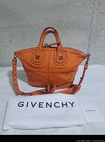 Front view of orange Givenchy Nightingale mini tote with shoulder strap, dust bag and booklet visible
