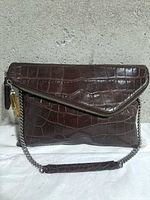Front view showing crocodile-embossed leather, envelope flap, diagonal zipper, chain strap