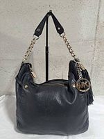 Front view of black pebbled leather Michael Kors hobo bag showing chain strap, tassel and MK charm