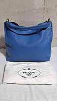 Front view of blue Prada Vitello Daino bag with dust bag displayed