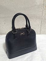 Front three-quarter view of black domed handbag showing hardware and handles