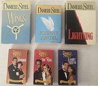 Group shot of three Danielle Steel hardcover books and three VHS movies