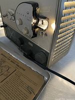 Front view of projector showing lens assembly, control dials, power cord and lamp illuminated