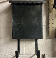 Front view of black metal mail box showing scalloped flap and two hooks