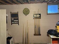 Wall view with dartboard, scoreboard, cue rack, loose cues