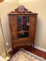 Front view of walnut china cabinet showing glass door, carvings, drawer and casters