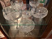 Front view showing two crystal bowls and pedestal cake stand on glass shelf