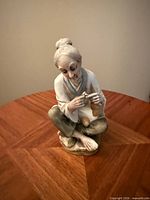 Front view of porcelain figurine seated cross-legged, holding small object