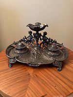 Front view of ornate cast metal double inkwell showing both lidded wells and cherub centerpiece