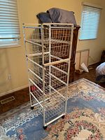 Full view of tall white rolling wire basket organizer showing four baskets and casters