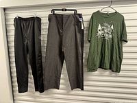 Three clothing items hanging: black athletic pants, grey dress pants, green graphic T-shirt