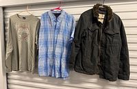 Three garments hanging: jacket, plaid shirt, graphic tee