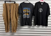 Overview of jogger pants and two T-shirts hung against wall