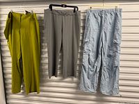 Three pairs of pants hanging: green, grey, light blue cargo