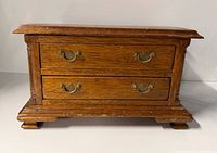 Front view showing wooden jewelry box, two brass handles, molded base and feet