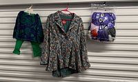Women’s floral blazer, toddler outfit, and bagged purple plush set hanging side by side