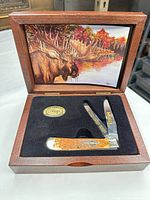 Open wooden display box showing knife, medallion, and moose artwork on lid