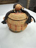 Overall view of basket front showing doll finial, lid, woven reed body and colour accents