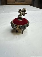 Front view showing cherub finial, red velvet cushion, ornate metal sides and legs