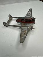 Angled top view showing overall airplane, red cockpit and axle with one wooden wheel