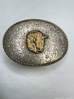 Front view of oval buckle showing scroll engraving, brass horse head, rope edge