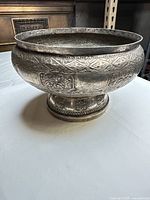 Side view of large silver-plated footed bowl showing engraved and repoussé decoration