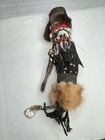 Full view of doll showing wood handle, fur trim, leather fringe and abalone shell pendant