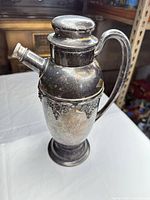 Full left-side view of silver-plated lidded pitcher showing handle, spout and decorative band