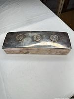 Top view of rectangular silver-plated trinket box showing three coin medallions and tarnish