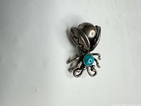 Front view of silver-tone insect brooch showing turquoise stone and legs