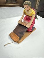 Front view of cloth doll on wood base with pull string and wooden roller board
