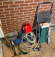 Group view against brick wall: ladder, gas can, garden seat, hose, screen, hoe, cultivator, C-clamp