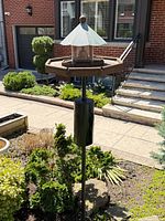 Full view of freestanding bird feeder with pole and garden surroundings
